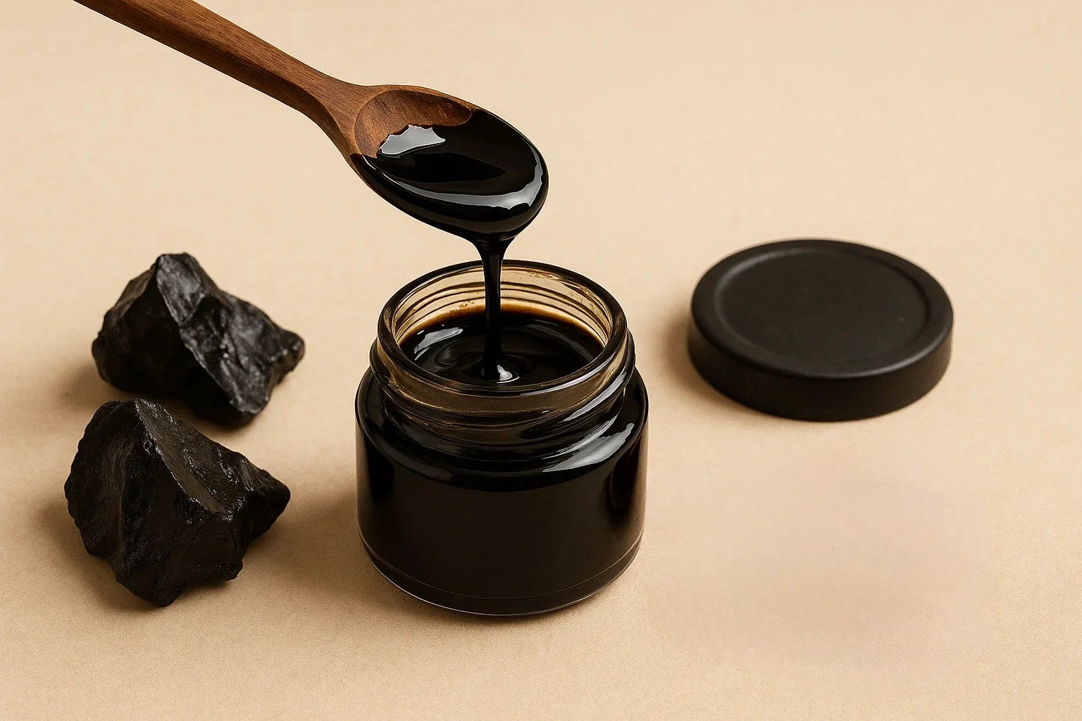 Jar of Kashmiri Himalayan Shilajit with a wooden spoon and pieces of raw Shilajit rocks on a beige background