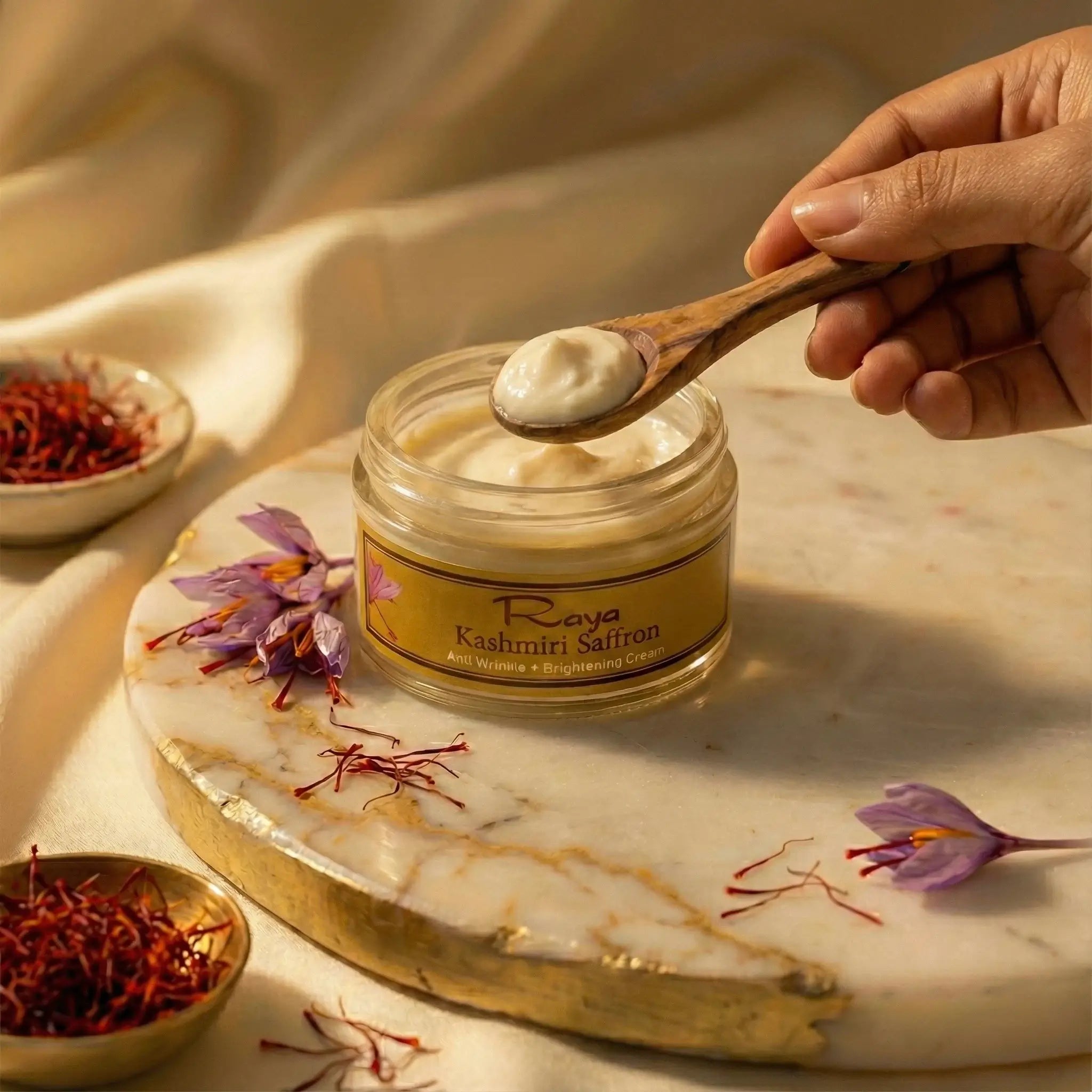 Jar of cream with a wooden spoon on a marble surface, surrounded by saffron and flowers.
