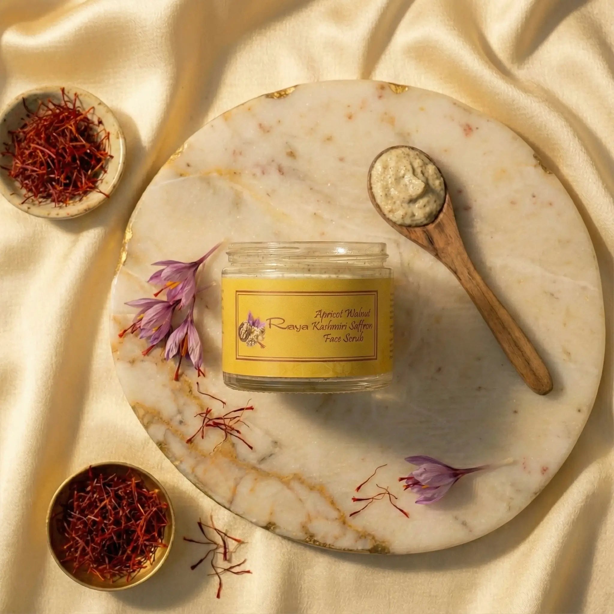 Jar of Raya face scrub on a marble tray with saffron and flowers, on a beige fabric background