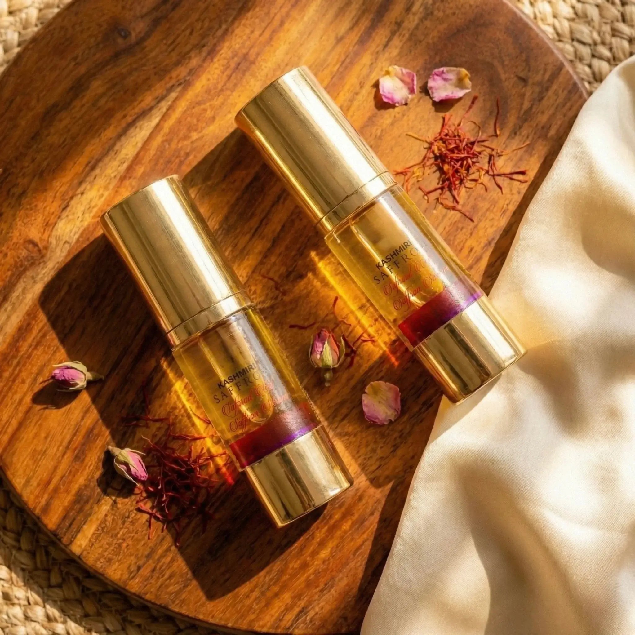 Two gold Saffron Serum bottles with a purple liquid on a wooden surface with dried flowers.
