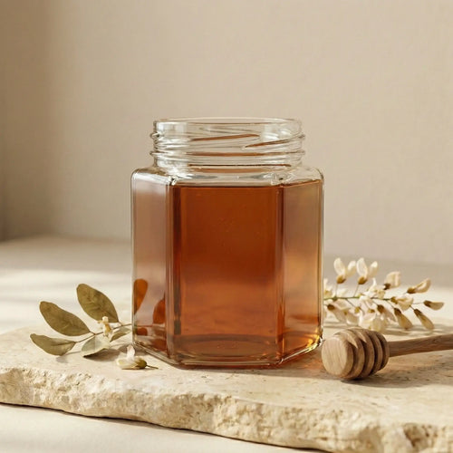 Clear glass jar of Kashmiri Sidr Honey with a wooden honey dipper on a light surface.