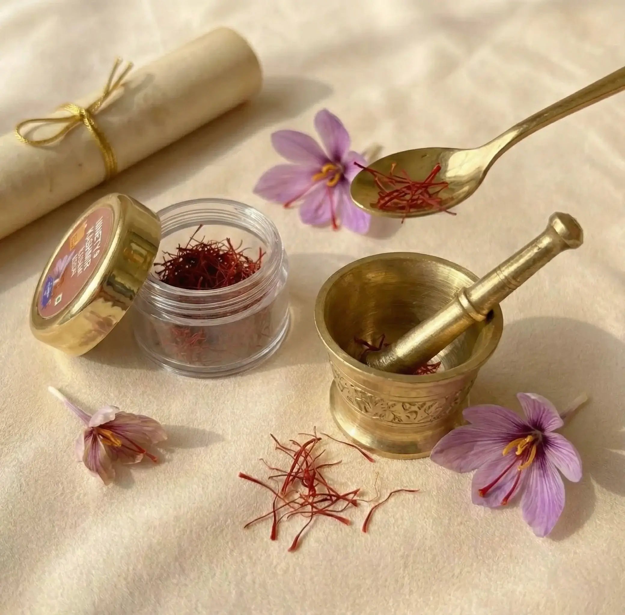 Saffron threads in a jar with a spoon, mortar, and pestle on a light fabric background.
