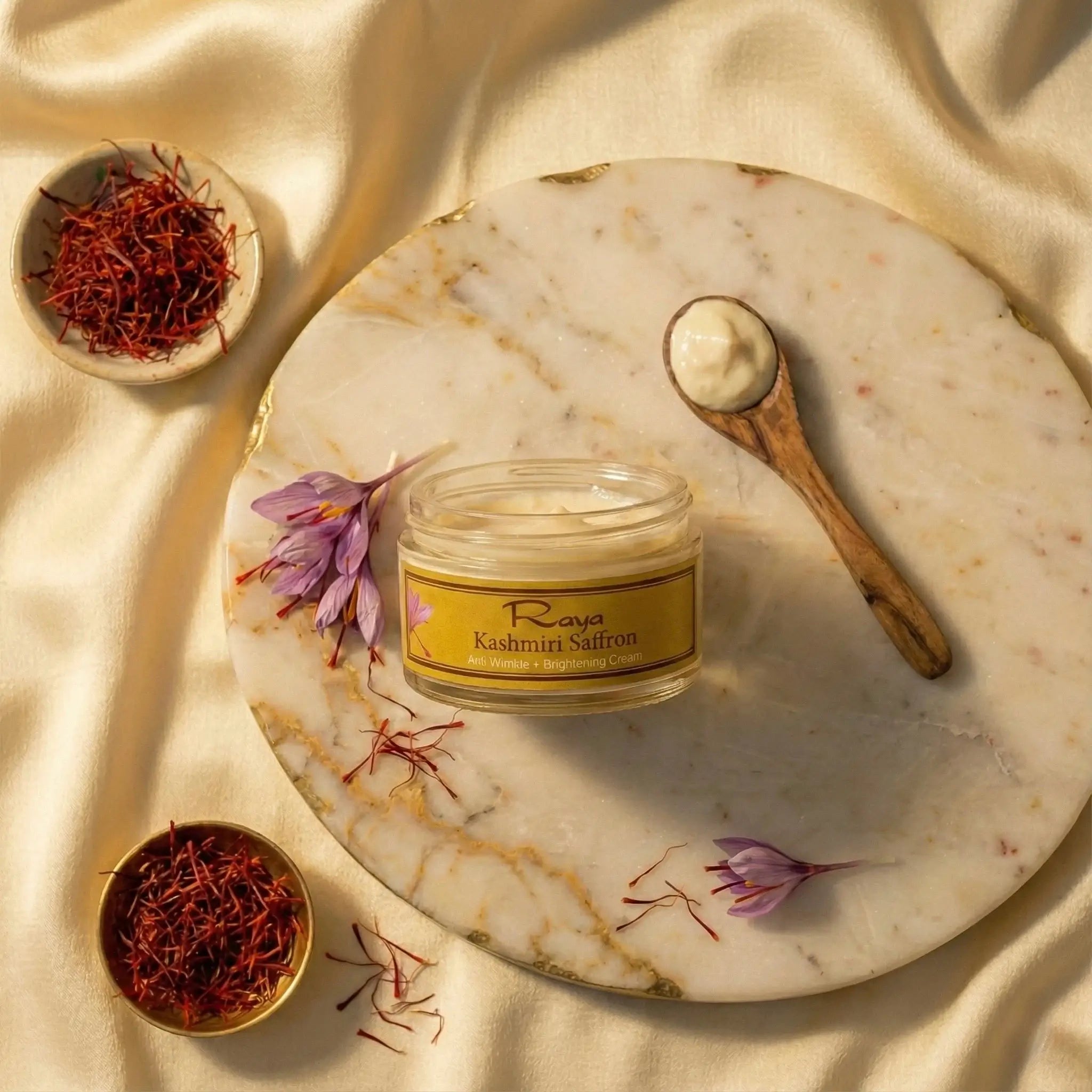 Jar of Rava Kashmiri Saffron cream with a wooden spoon and saffron threads on a marble surface.