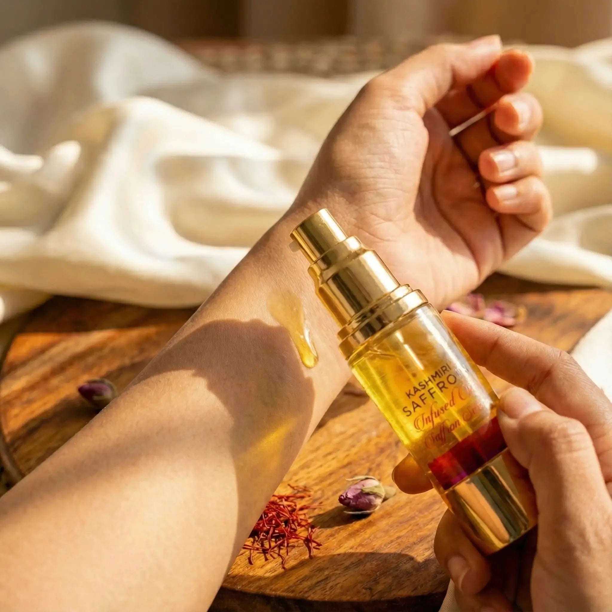 Hand holding a gold and red bottle labeled 'Kashmiri Saffron Serum' over a wooden surface with saffron strands.