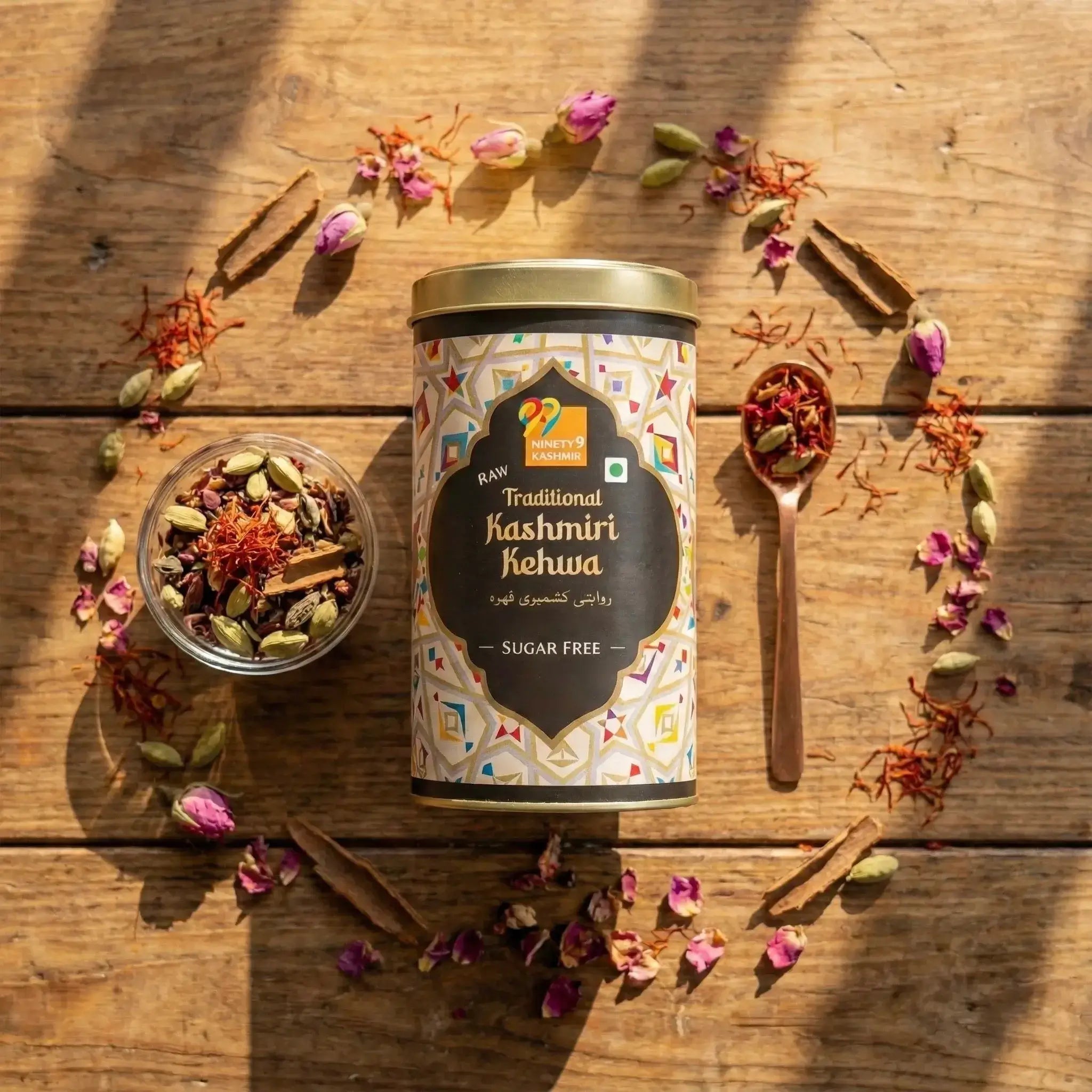 Traditional Kashmiri Kehwa tea canister on a wooden surface with tea leaves and flowers around it.